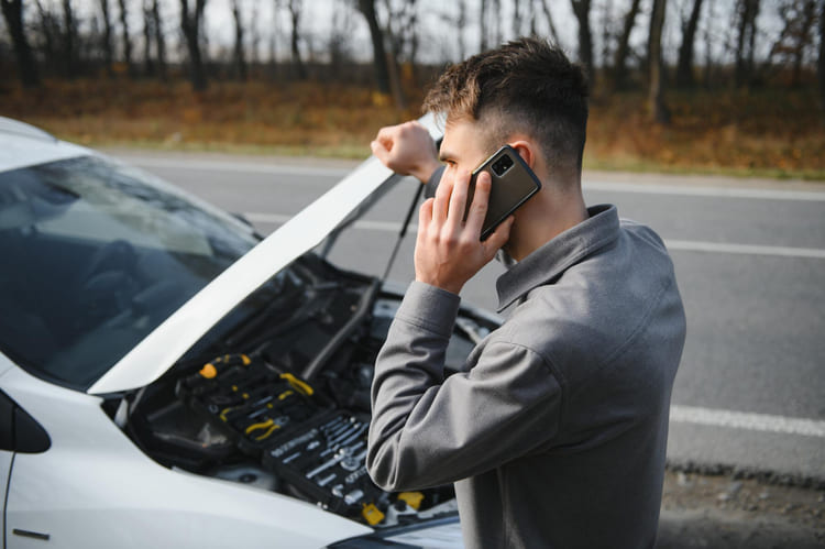 Șofer sunând la tractări auto lângă mașina defectă